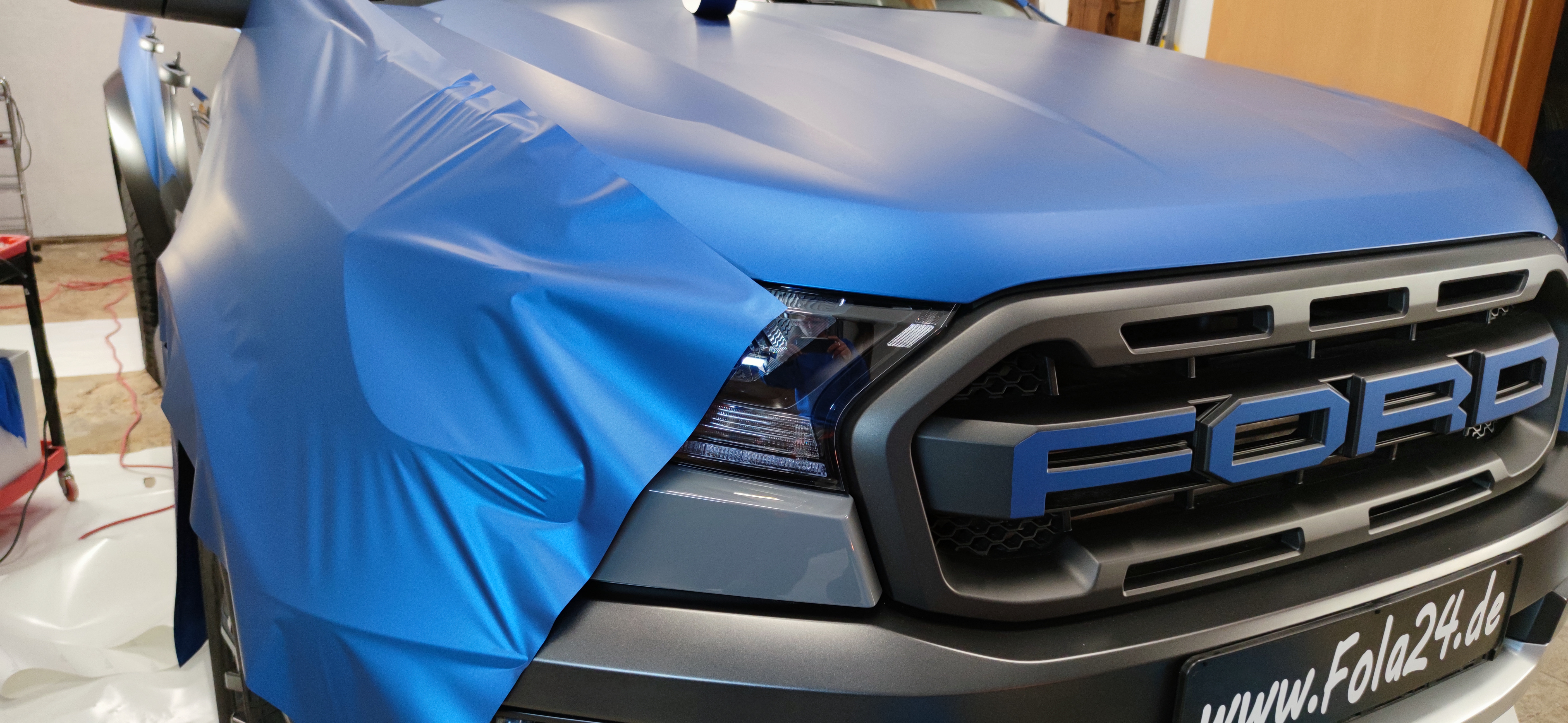 Hier zeigen wir einen Ford während der Folierung. Die Motorhaube ist bereits foliert und nun wird der Kotflügel foliert. Image